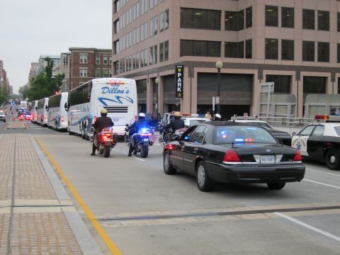 1991 Ford LTD Crown Victoria - black police cruiser and motorcycle escort accompany a line of Dillon's tour buses down a downtown street with other cruisers nearby.