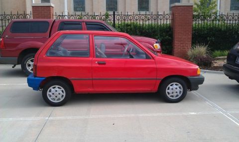 1991 Ford Festiva - A red hatchback is parked in a lot with other vehicles nearby.
