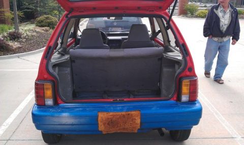 1991 Ford Festiva - Rear view of a red hatchback with a blue bumper and an open trunk. A second vehicle is visible in the background.