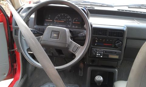 1991 Ford Festiva - The interior of a 1991 Ford Festiva, the dashboard, steering wheel with Ford emblem, and center console.