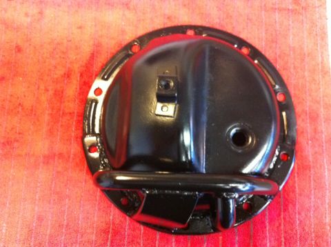 1987 Suzuki Samurai - A black differential axle cover is shown against a red textured background. The cover has several mounting holes and a small metal bracket…