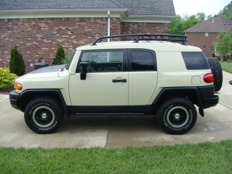 2010 Toyota FJ Cruiser - Side view of a white 2010 Toyota FJ Cruiser parked on a paved surface with grass and a house in the background.