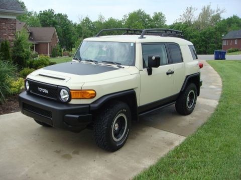 2010 Toyota FJ Cruiser - A tan Toyota FJ Cruiser is parked on a concrete driveway in front of a residential house.