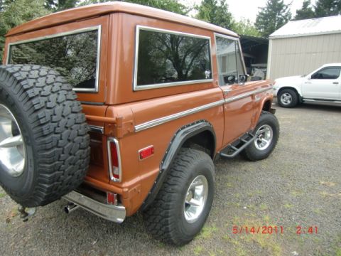1973 Ford Bronco - Rear view of a 1973 Ford Bronco, with a white pickup truck in the background.