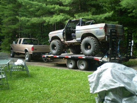 1979 Ford Bronco - A lifted Bronco is transported on a trailer, pulled by a pickup truck, with trees in the background.