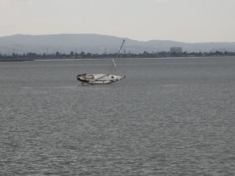 1991 Ford Bronco - A damaged sailboat is adrift in calm waters under an overcast sky.