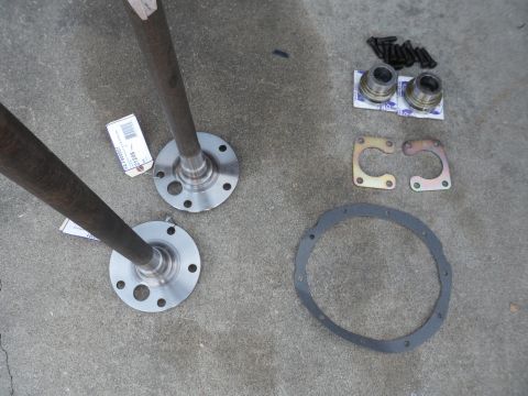 1991 Ford Bronco - Axle shafts, bearing kits, and a gasket are arranged on a concrete surface, likely for a vehicle repair or upgrade.