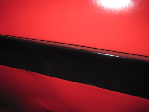1979 Ford Bronco - A close-up view shows a section of a red vehicle's exterior, a black accent strip.
