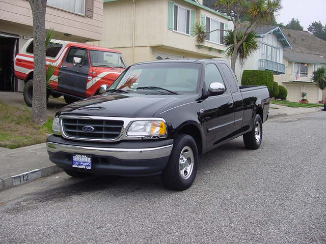 Black 2001 Ford F-150 pickup truck parked on street, red Bronco in background