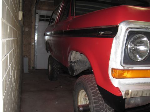 1979 Ford Bronco - Close-up of a red SUV's front corner, parked indoors with a garage door in the background.