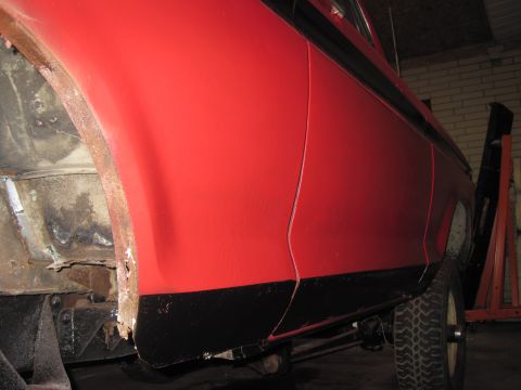 1979 Ford Bronco - Side view of a red vehicle showing rust damage near the wheel well and black trim along the lower body.