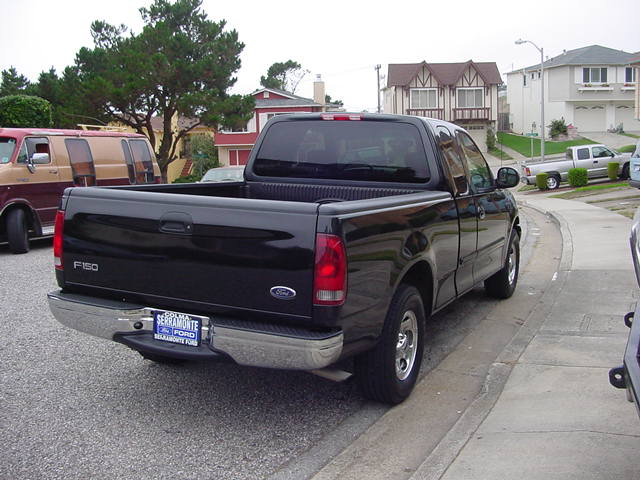 Black Ford F-150 extended-cab pickup parked on a suburban street, rear three-quarter view