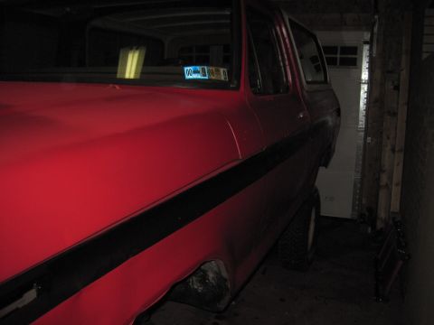 1979 Ford Bronco - A red SUV with a black stripe is parked in a garage, showing a partial view of its side and front.