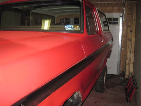 1979 Ford Bronco - A red 1979 Ford Bronco is parked in a garage, showing its side and front quarter panel.
