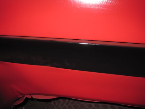 1979 Ford Bronco - Close-up of a red vehicle body panel a black trim accent. A tire is visible at the bottom.