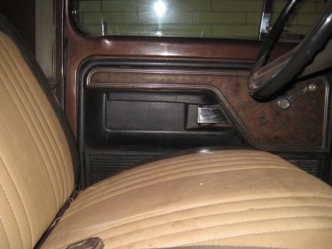 1979 Ford Bronco - The interior door panel and seat of a vehicle are shown, brown and tan upholstery with wood-grain accents.