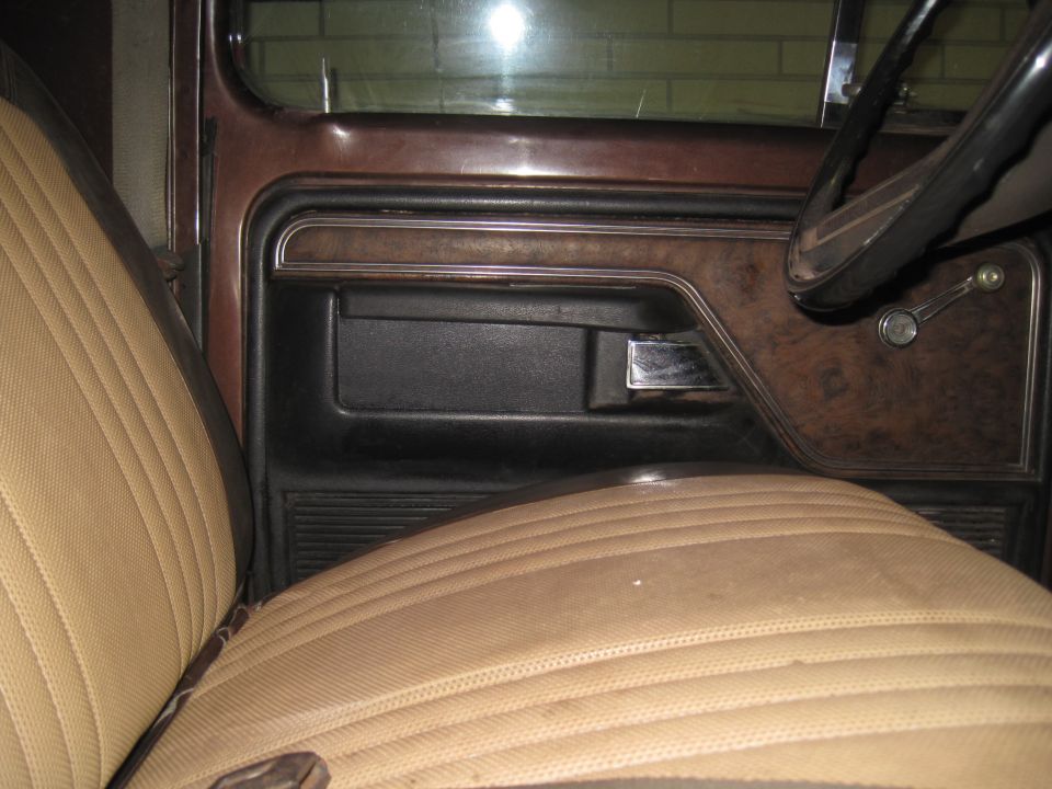 Passenger side door panel with wood grain trim, black armrest, and chrome handle. Tan seat with stitching visible