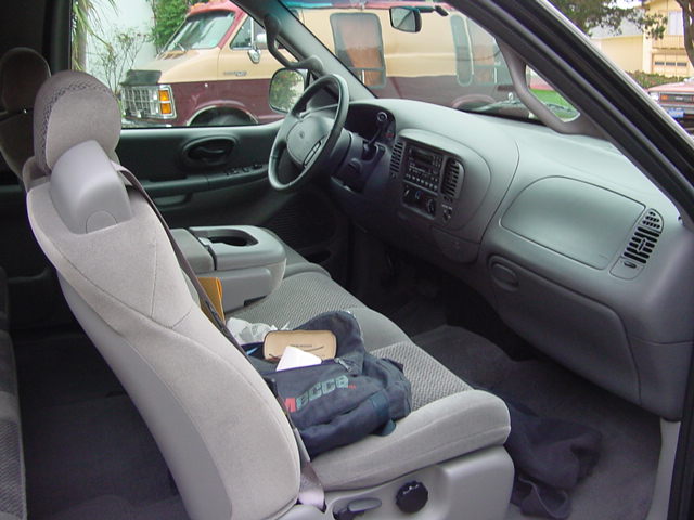 Interior of a 2001 Ford F-150 showing the dashboard, steering wheel, and seats. A jacket is on the passenger seat