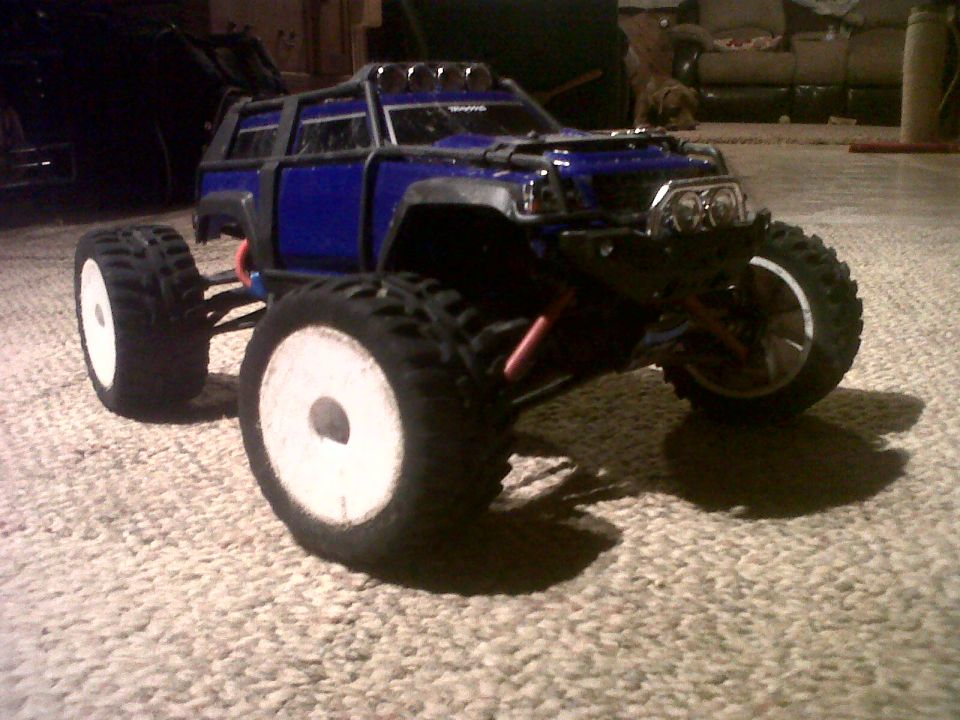 Blue RC monster truck with large tires and roll cage on carpet