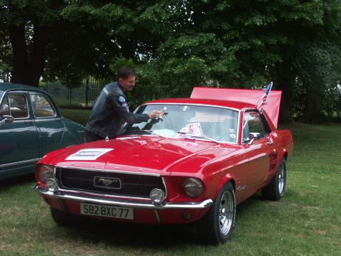 1977 Pontiac Trans Am - A man cleans the windshield of a red 1967 Ford Mustang parked next to a green car.