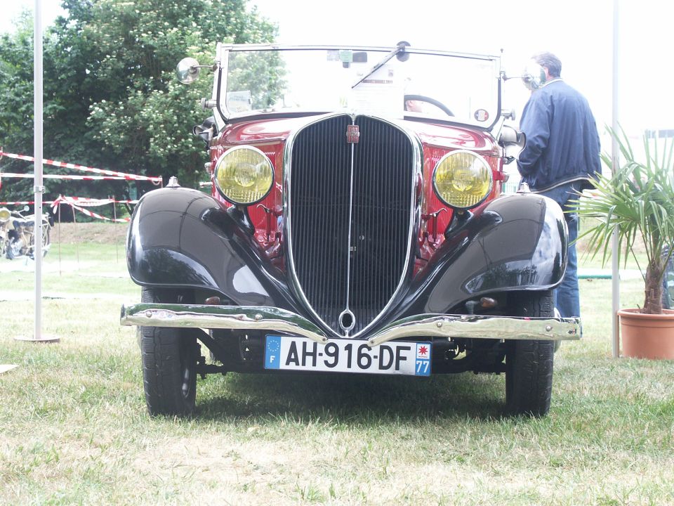 Front view of a red and black vintage car with yellow headlights and license plate AH-916-DF