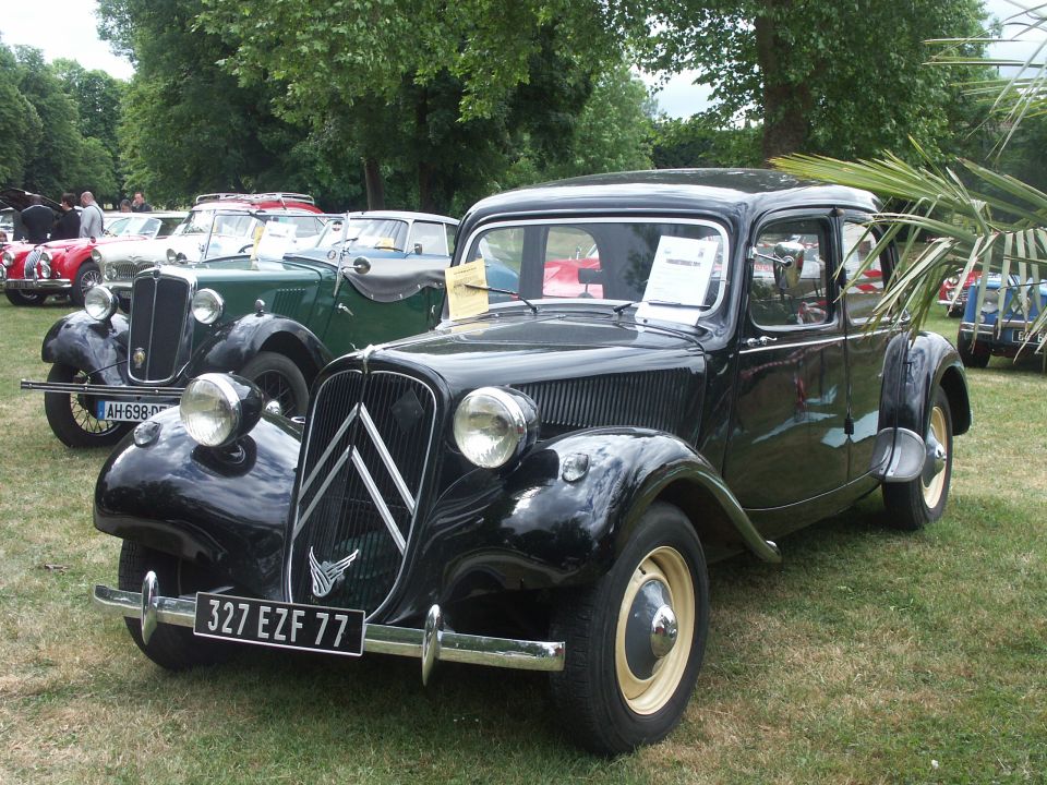 Black Citroën Traction Avant with license plate 327 EZF 77 parked on grass, other vintage cars behind it