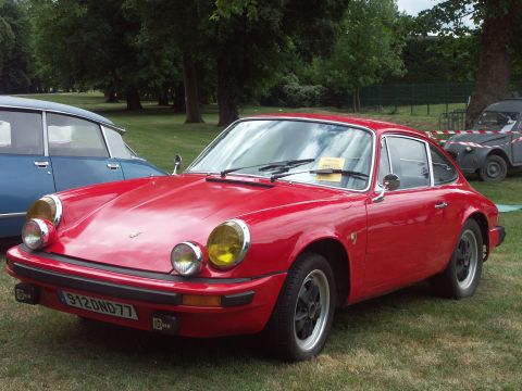 1977 Pontiac Trans Am - A red Porsche 911 is parked on grass with other vehicles in the background.