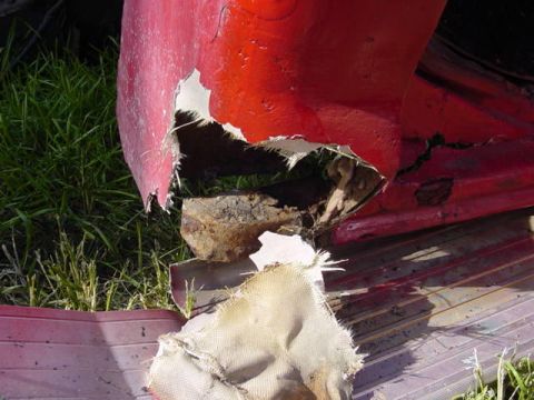1992 Ford Bronco - Damaged red vehicle panel shows significant structural compromise and rust.