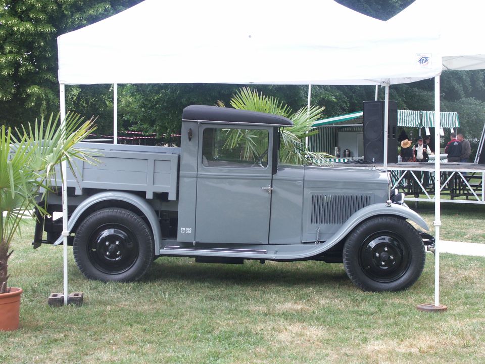 Gray pickup truck with a flatbed, black wheels, and a black roof, viewed from the side under a white tent