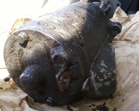 1976 Ford Torino - A heavily soiled starter motor is shown in this close-up view, likely removed from a vehicle for repair or replacement.
