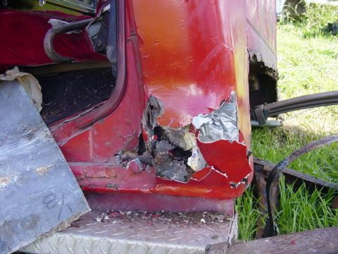 1992 Ford Bronco - The rear quarter panel of a red truck exhibits severe rust and damage, with exposed metal and silver tape repairs.