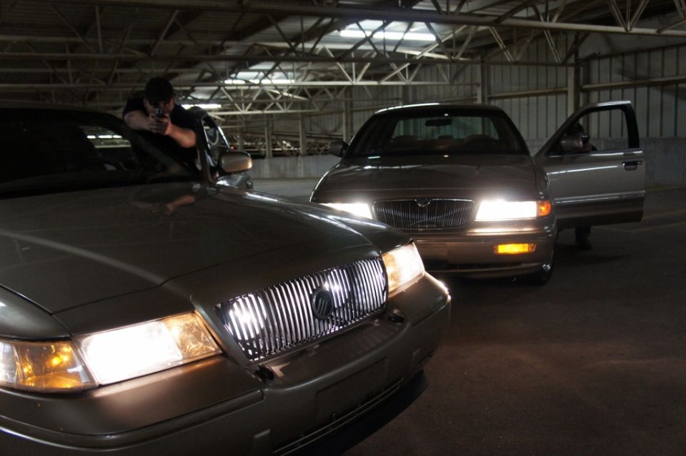 Two tan 2000 Mercury Grand Marquis sedans parked in a garage, one with its driver's door open