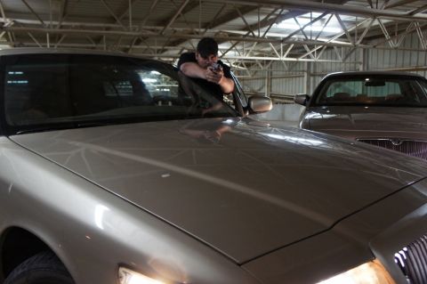 2000 Mercury Grand Marquis - A man aims a handgun from the driver's seat of a 2000 Mercury Grand Marquis, with a second vehicle visible in the background.