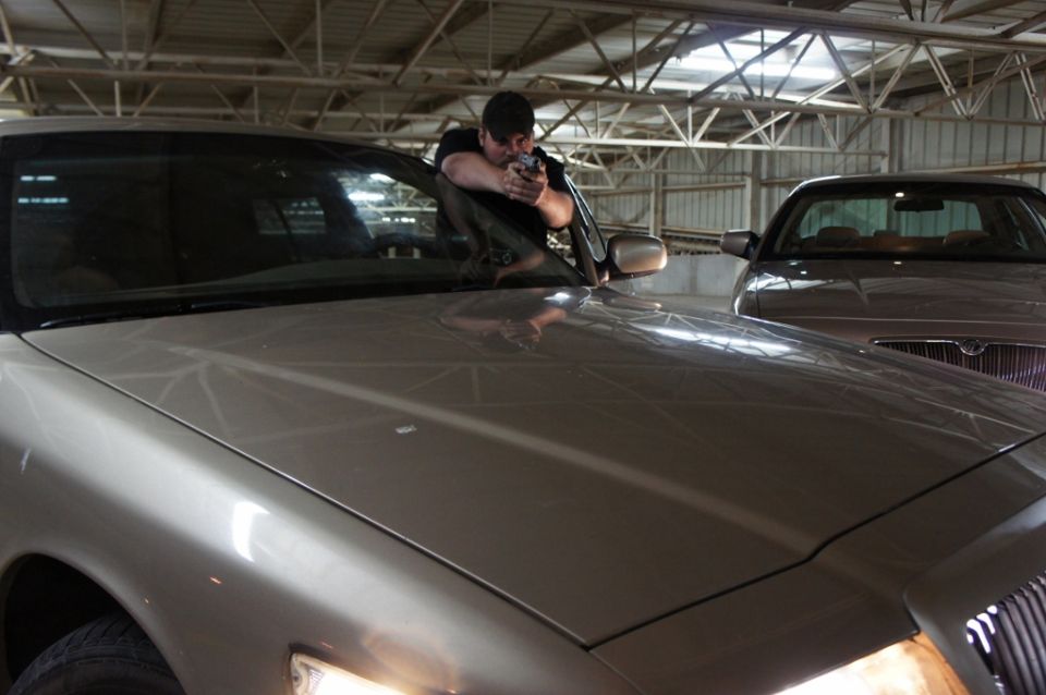 Man aiming handgun from a 2000 Mercury Grand Marquis, with another car behind