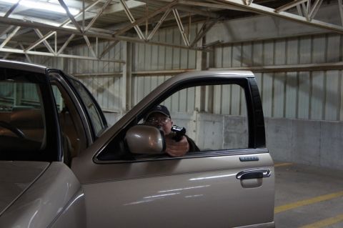 2000 Mercury Grand Marquis - A man points a handgun from the open driver's side window of a tan sedan in a parking garage.