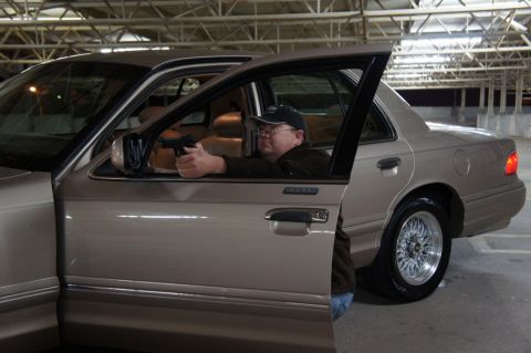 2000 Mercury Grand Marquis - A man with a handgun is seated in a tan 2000 Mercury Grand Marquis with the driver's side doors ajar.