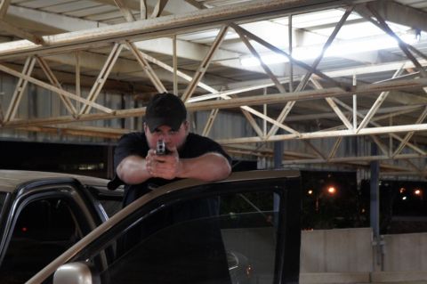 2000 Mercury Grand Marquis - A man aims a handgun from the interior of a car, leaning on the open door frame.