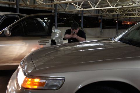 2000 Mercury Grand Marquis - A man aims a handgun while positioned between two vehicles in a covered parking area.