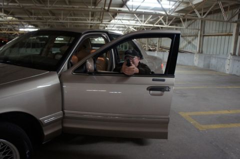 2000 Mercury Grand Marquis - A man aims a handgun from the driver's seat of a tan sedan in a parking garage.