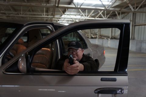 2000 Mercury Grand Marquis - Man aims handgun from inside a 2000 Mercury Grand Marquis during a garage meet.