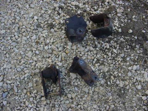 1992 Ford Bronco - Several old, corroded metal brackets lie on a bed of gravel.