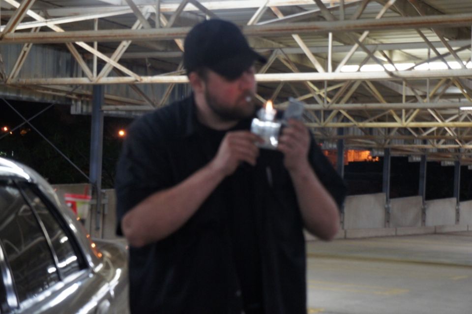 Man in black shirt and cap lighting a cigarette with a lighter
