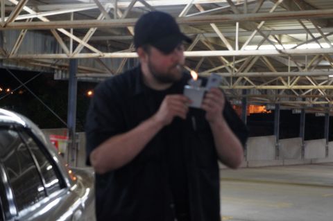 2000 Mercury Grand Marquis - A man lights a cigarette under a covered structure with a car visible on the left.