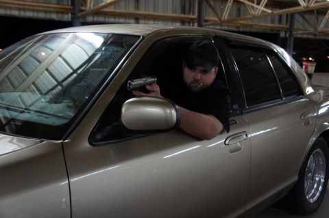 2000 Mercury Grand Marquis - A man with a handgun is visible through the driver's side window of a gold sedan.
