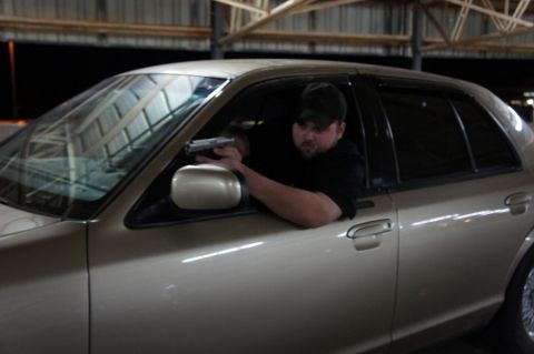 2000 Mercury Grand Marquis - A man points a handgun from the driver's side window of a tan 2000 Mercury Grand Marquis.