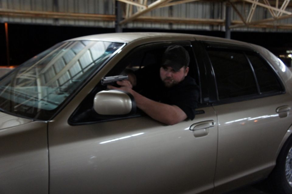 Side view of a tan 2000 Mercury Grand Marquis with a man holding a handgun out the window