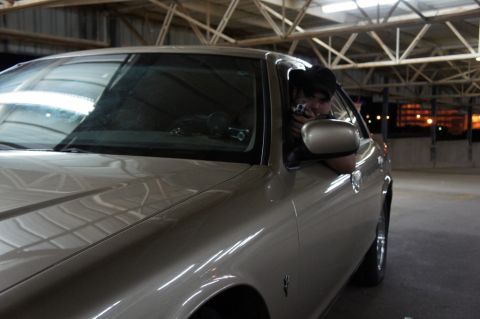 2000 Mercury Grand Marquis - A person aims a camera from the driver's seat of a tan sedan parked in a garage.