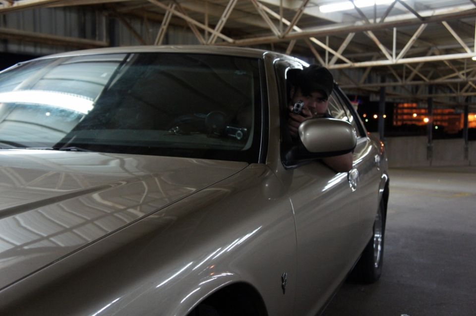 Tan sedan with a person in the driver's seat holding a camera out the window