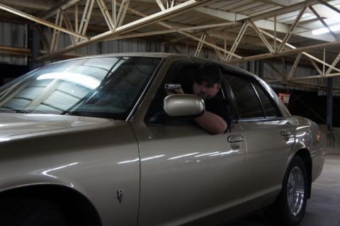 2000 Mercury Grand Marquis - A man holds a handgun while seated in the driver's seat of a tan 2000 Mercury Grand Marquis inside a garage.