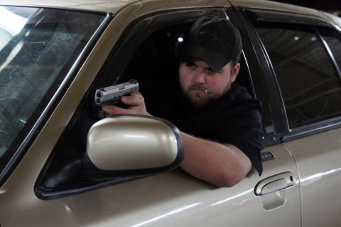 2000 Mercury Grand Marquis - A man holds a handgun out the window of a tan 2000 Mercury Grand Marquis.